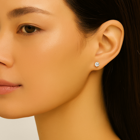 "Close-up profile of a woman wearing small, round, brilliant-cut solitaire crystal stud earrings in a silver-tone setting.