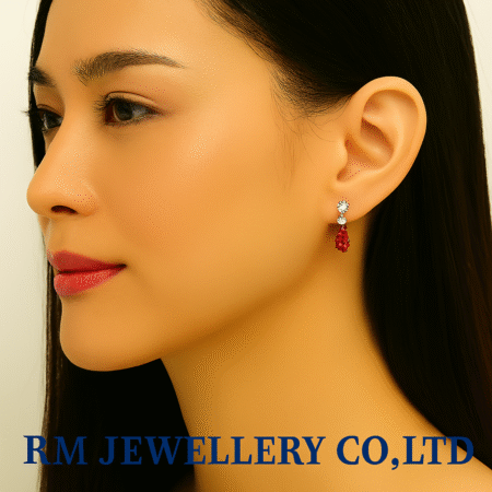 "Close-up profile of a woman wearing small drop earrings featuring a clear round stud connected to a dangling oval or pear-cut red gemstone.