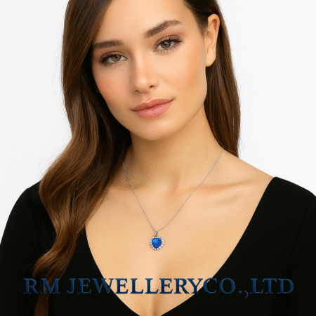"Woman wearing a silver chain necklace with a large, heart-shaped, deep blue pendant surrounded by small clear stones on a white background. The text 'RM JEWELLERY CO., LTD' is visible at the bottom."